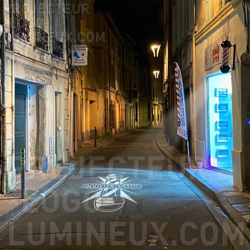 Beleuchteter Friseursalon durch Projektion des beleuchteten Logos auf dem Bürgersteig